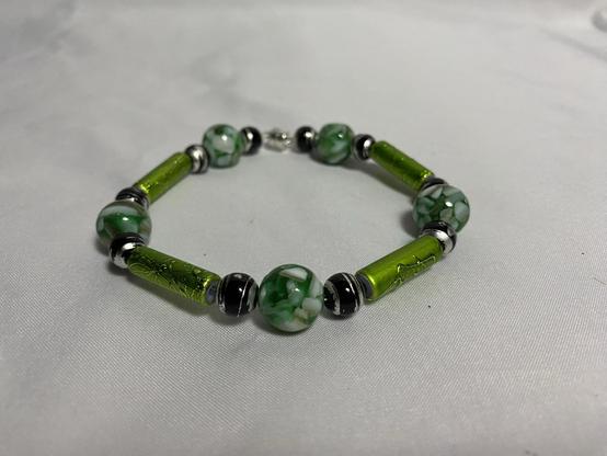 A green and black beaded bracelet featuring patterned glass beads and metallic accents on a light background.
