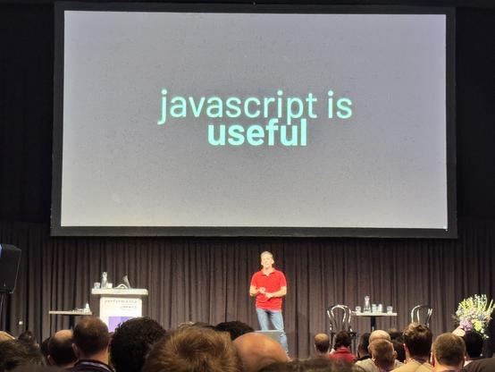 Daniel Roe on stage, with a big screen that says “javascript is useful”