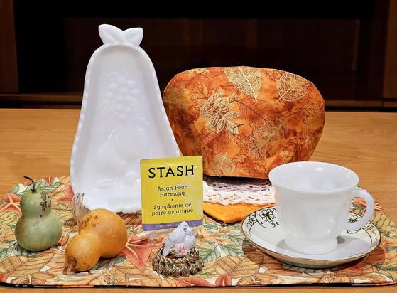 A tea tableau in warm orange and yellow with green accents and vintage white milk glass pieces forming an Autumn setting with pears as the theme. The tea is Asian Pear green tea from Stash of Oregon.