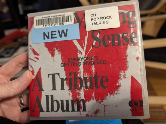 Color photo of a music CD with the words NEW Sense A Tribute Album in black letters against an abstract red and tan background