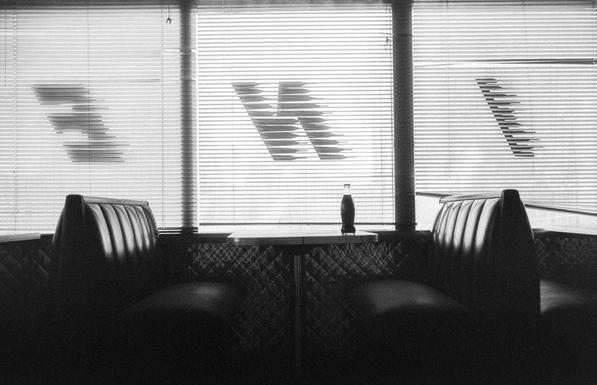 black and white image of a diner booth with a bottle of coke on the table