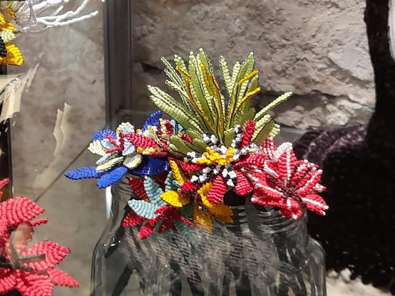 A collection of perlage flowers in a museum: the flowers are made with colourful glass rocailles. The beads are grouped in parallel rows to form leaves and petals. Bad photo quality: It was behind glass with too many visitors reflecting.