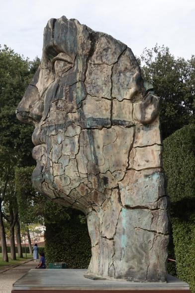 A large sculpture of a face, seen from the side. Large cracks run through the face.