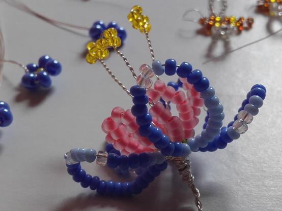 Fantasy perlage flower in blue and rose with long yellow stamen. The flower is worked on the finest silver wire. In terms of colour, it is characterised by varying degrees of transparency: many beads are opaque, some are made of frosted glass and some, such as the pollen, are transparent for greater brilliance.