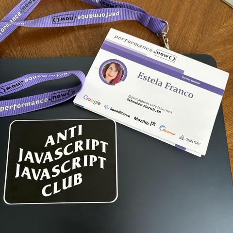 The image shows a name badge and lanyard from the performance.now() conference placed on a black laptop. The badge displays the name “Estela Franco,” with the title “Former Speaker” and affiliation “Schneider Electric, ES,” along with a mastodon handle “@guaca@toot.cafe”. Next to the badge is a black sticker with white text reading “ANTI JAVASCRIPT JAVASCRIPT CLUB.”