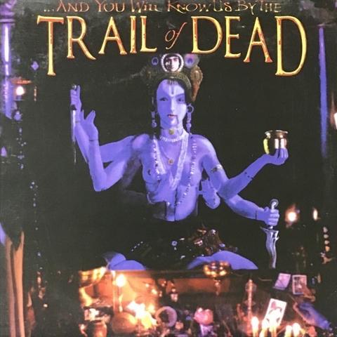 An album cover with an artistic depiction of a blue-skinned figure seated among candles and offerings, with the text "...And You Will Know Us by the Trail of Dead" prominently featured at the top.