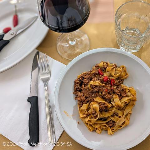 A plate of Tagliatelle with ragù and a glass of Lambrusco wine.