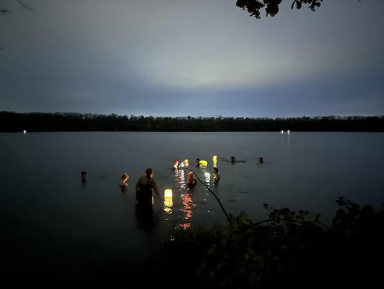 Menschen in Badekleidung ziehen am Abend mit Laternen in eine See.