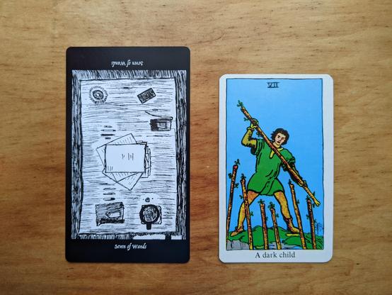 The Seven of Wands from the Elsewhere Tarot, showing a top-down view of a desk, with a loose manuscript on it, seven pens arrayed, and a cup of coffee, alongside the Seven of Wands from a janky, bootleg RWS deck, showing a dude backed against the edge of a precipice, defending himself with his living wand against six living wands with unseen wielders coming at him.