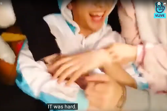 blurry screen capture of Seungmin's torso and the lower half of his happy face. Several other people's hands are reaching for his midsection. Caption: it was hard