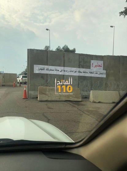 A warning sign mounted on a concrete barrier, advising against trespassing and informing drivers about traffic regulations. The scene shows a clear road with traffic cones and vehicles, indicating a controlled area.