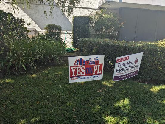 A lawn sign with a library, books, and main text "YESonPL", subtitled with "Save Pasadena's Library". Also a lawn sign for the re-election of Tina Wu Fredericks to the Pasadena Unified School Board.
