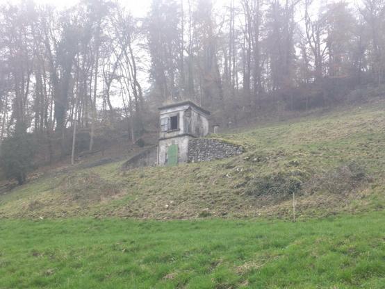 Ein kleines, altes, zweistöckiges Gebäude am Hang. Unten hat es eine eiserne Tür, oben ein offenes Fenster. Dem rauschen nach dient es der Wasserversorgung.