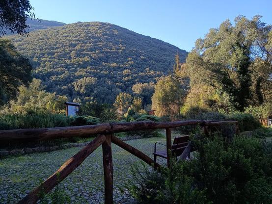 Area di ristoro nel verde, con panchine, pannelli informativi e vegetazione di basso e alto fusto. L'area è delimitata da una palizzata in legno.