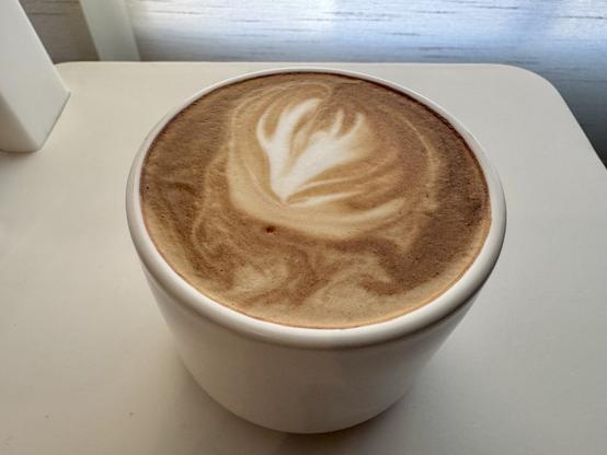 Small white coffee mug filled with a frothy cappuccino sitting on a small white chair.
