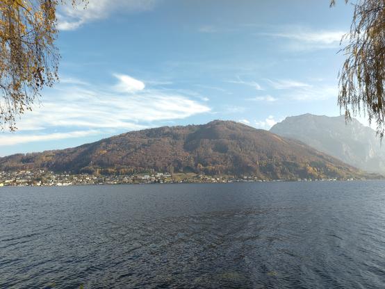 Blick über den Traunsee, dahinter der bewaldete #Grünberg, rechts daneben etwas höher der #Traunstein, hauptsächlich Fels. Blauer Himmel mit ein paar vereinzelten Wölkchen, sonniges Wetter.