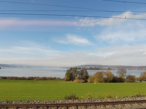 Foto. Blauer Himmel mit etwas Wolken, ein See und ein Gleis.