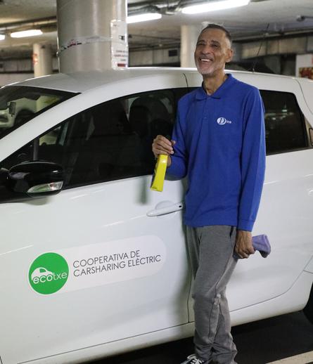 En Bonifacio posa davant la càmera amb un Ecotxe just darrera, a la porta del conductor. A les mans té un esprai i un pedaç amb els que neteja els vehicles.