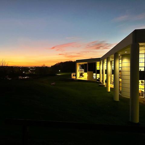 The sky in sunset colors, a dark foreground and a building with lights in the windows to the right.