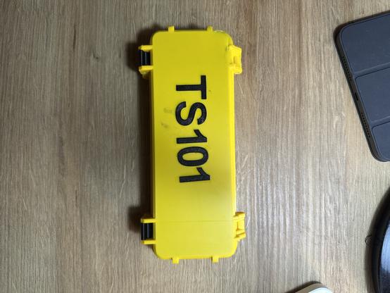 Bild 2: Geschlossene gelbe Kunststoffbox mit der Aufschrift “TS101” auf dem Deckel.