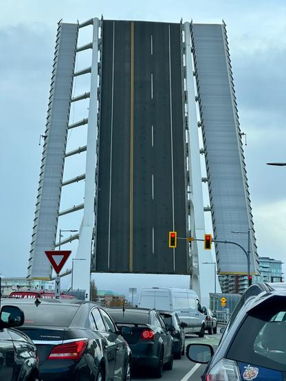 In the background, a drawbridge raised vertically; in the foreground, cars waiting for the bridge to be lowered.