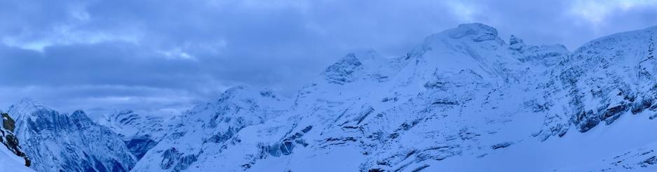 A panoramic view of snow-covered mountains under a cloudy sky, showcasing a serene winter landscape.