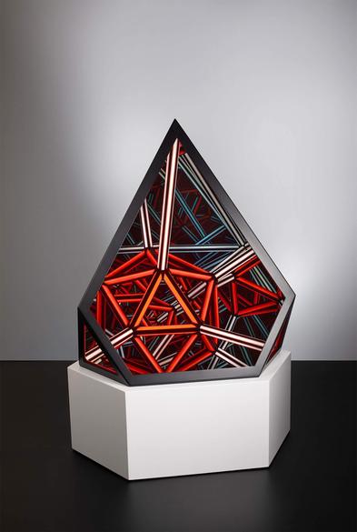 Geometric art piece with a triangular form, featuring interlocking red, white, and teal lines, displayed on a hexagonal white pedestal.