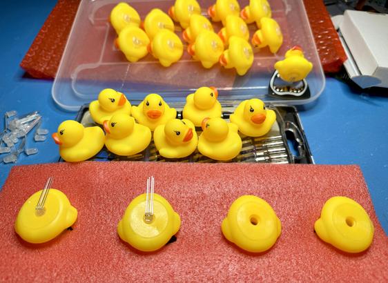 Flock of about 20 small yellow rubber ducks, at various stages of getting an LED installed into the hole on their bottom