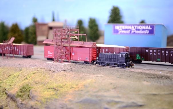 A tiny N scale black switcher is loading some sawdust cars at a sawmill.