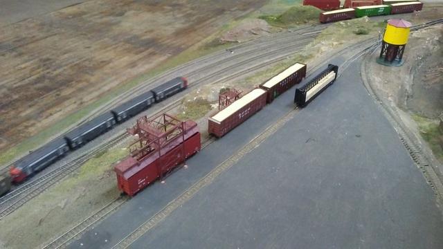 Several N-scale lumber cars are left on a siding while a Southern Pacific train passes by.