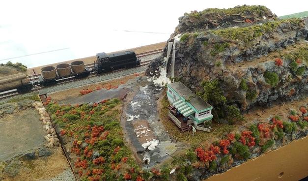 A small black switcher pulls some flatcars past a waterfall on our T-TRAK layout.