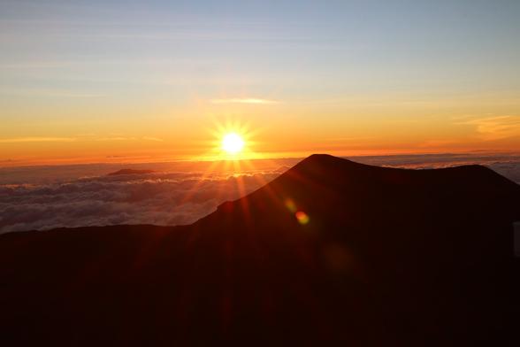 Sunset from the summit of Mauna Kea in October 2024. A small aperture of f16 has created a sunburst that reaches from the sky to join a lens flare below the silhouetted foreground cinder cone. The horizon is slightly slanted as I’ve turned the tripod-mounted camera from my main composition of telescopes at the summit.