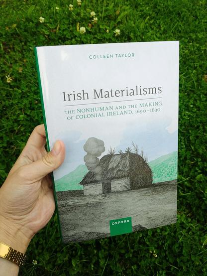 Holding the book "Irish Materialisms" in front of a meadow on which grows clover