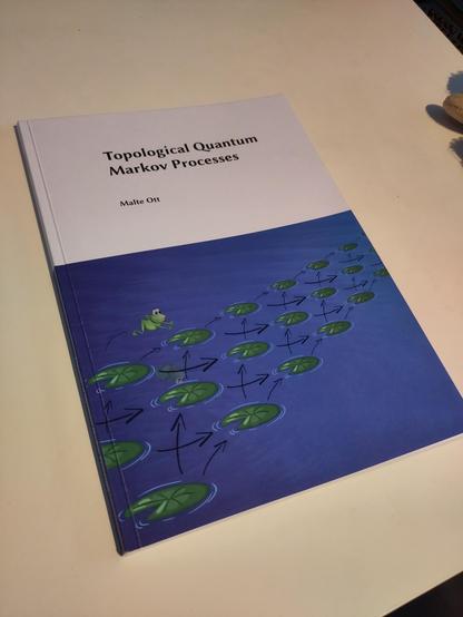 A photo of a Ph.D. thesis titled "Topological Quantum Markov Processes". The cover shows a frog jumping between leaves on a water surface connected by arrows.