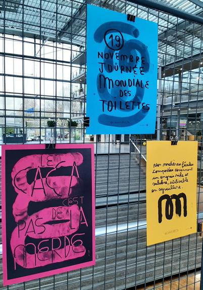 Un panneau de l'exposition à l'école des ponts, avec l'affiche pour la journée mondiale des toilettes ainsi que 2 autres, en dessous : "le caca c'est pas de la merde", sur fond rose, et l'explication "nos matières fécales compostées deviennent un engrais riche et salubre, utilisable en agriculture", sur fond jaune. Les deux contiennent en étron stylisé qui, sur la deuxième, ressemble à la lettre "m" manuscrite.