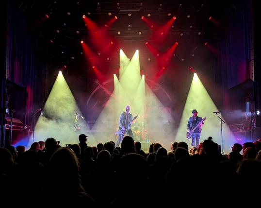 Sólstafir playing live. In the picture you can see the three string components of the band under three yellow light beams. In the center above, several red beams cross each other.