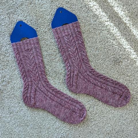 The Aviation Socks, knit in a heathery purple, have columns of wings flying over a stretchy ribbed background, which continue down into the heel and over the instep.