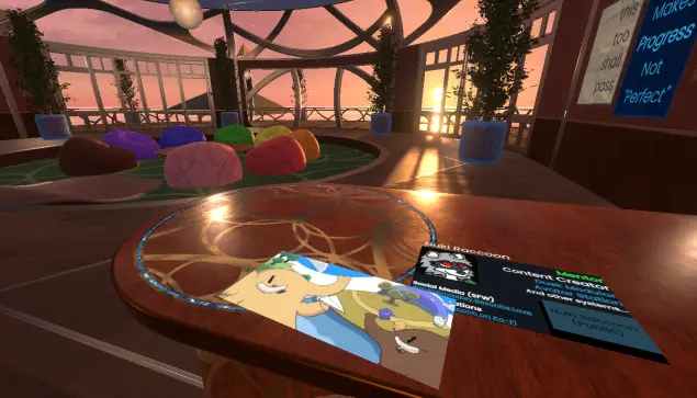 The main area of the support group world, with its rainbow of beanbag chairs, along with a counter where a card with my information on it sits under a card with Mastodon imagery on it: I encourage people to sign up for Fedi all the time.