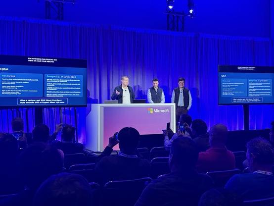 Maxim Lukiyanov Orhun Oezebak, & Jay Yang on stage at Microsoft Ignite giving a talk about how to improve the accuracy of GenAI applications with Azure Database for PostgreSQL. The blue mood lighting vibes are strong.