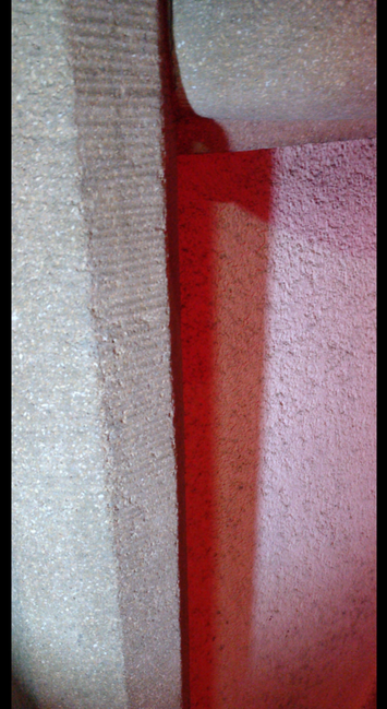 Eine verputzte Mauer mit einem leicht herausstehendem Pfosten aus Stein. Mehrere diffuse weiße Lichter und ein rotes Licht werfen Schatten mit parallel verlaufenden Kanten in Abstufungen zwischen rot und weiß.