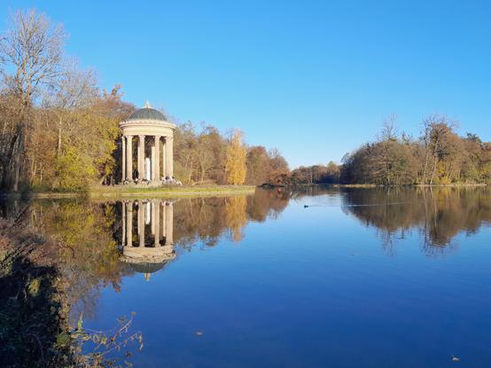 Ein weißes Tempel #Monopteros spiegelt sich im Wasser, darüber blauer Himmel