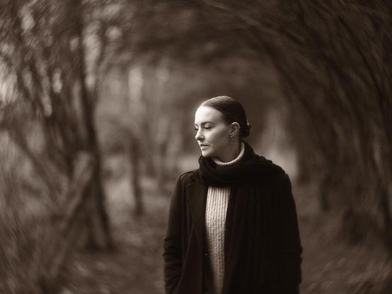 Young woman standing on a forest path, looking thoughtfully to the side.