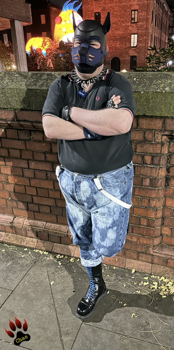 front view of a human pup, wearing skinhead gear (bleachers, polo shirt, blue-laced boots) standing in front of a wall, one foot against the wall, arms crossed, looking into the camera