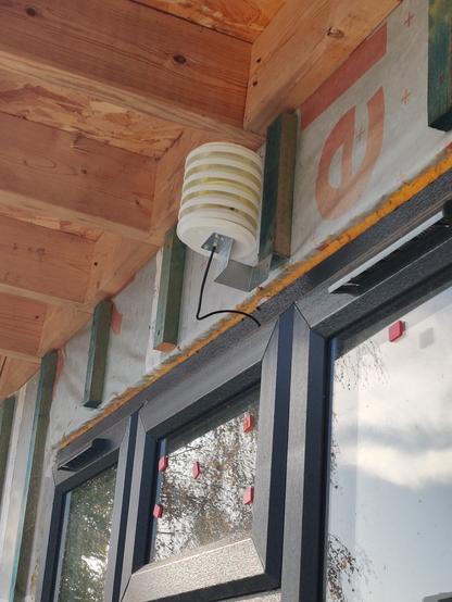 fully assembled Stevenson Screen made of layers of circular 3d printed white plastic so that the sensor inside is protected from the elements whilst still open to ambient temperature. it is sat below the overhanging roof.