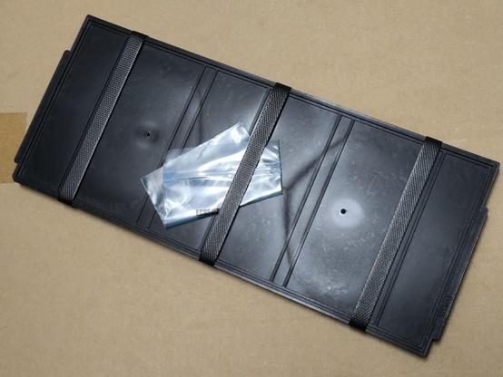 Black rectangular IC tray with a small plastic bag tucked under one  of the straps holding the tray together.