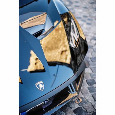 The picture shows a part of the front of a black lamborghini supercar, with the logo and the left front light. You can see the reflection of the Schelztor - an old tower of Esslingen - on the coating.