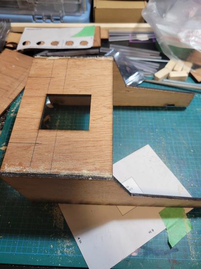The semblance of a wooden frame fro. The top down perspective. The top has a square cut out for wiring to go inside as the sides look like a rectangle with half of the shape having a 45 degree angle cut out of it while a elongated part remains to place piano type keys.