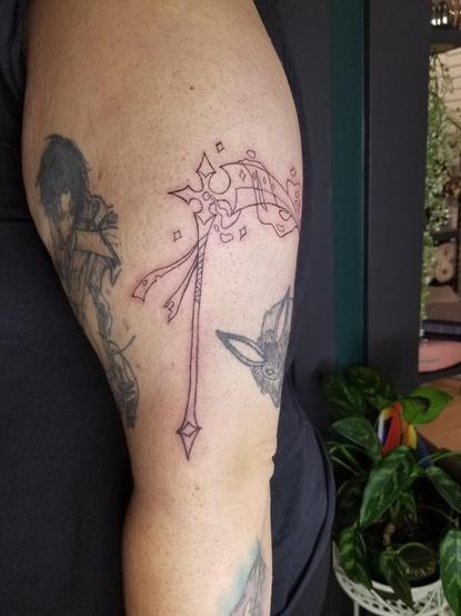 Photo of a large scythe tattoo (lines only) on a client's arm. The scythe has a tattered ribbon wrapped around its handle, and has a ghost wrapped around the blade, being summoned/sucked into a gem in the blades base.