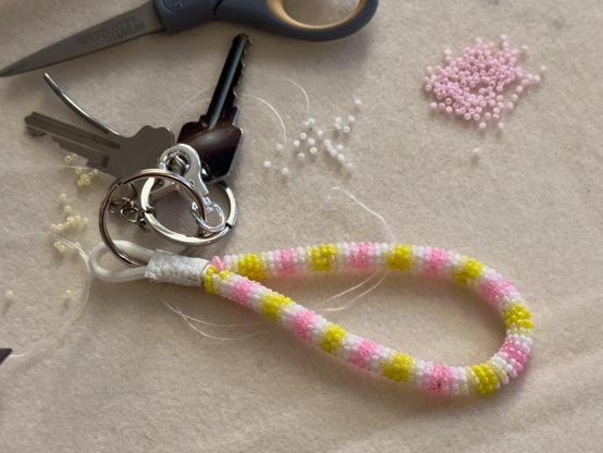 A pink, white, and yellow bead-wrapped keychain on a bead mat