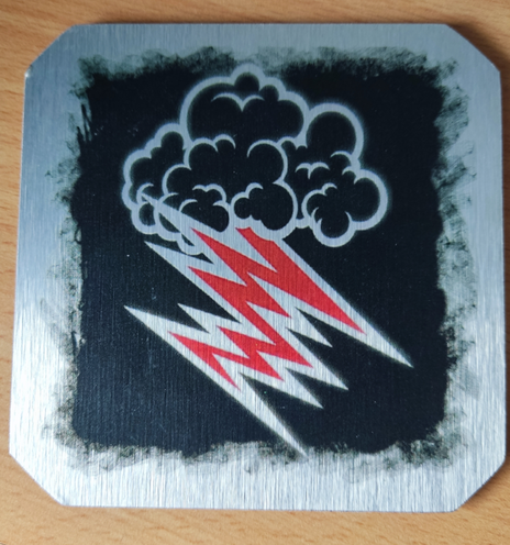 A Hellacopters' coaster printed in metal.
The classic Hellacopters logo of a black cloud throwing a red lighting bolt over a black background.